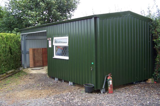 A small green building with a white window and open bay