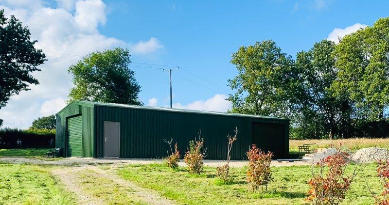 Wide-angle shot of a large green industrial shed in an open rural field under a bright sky.